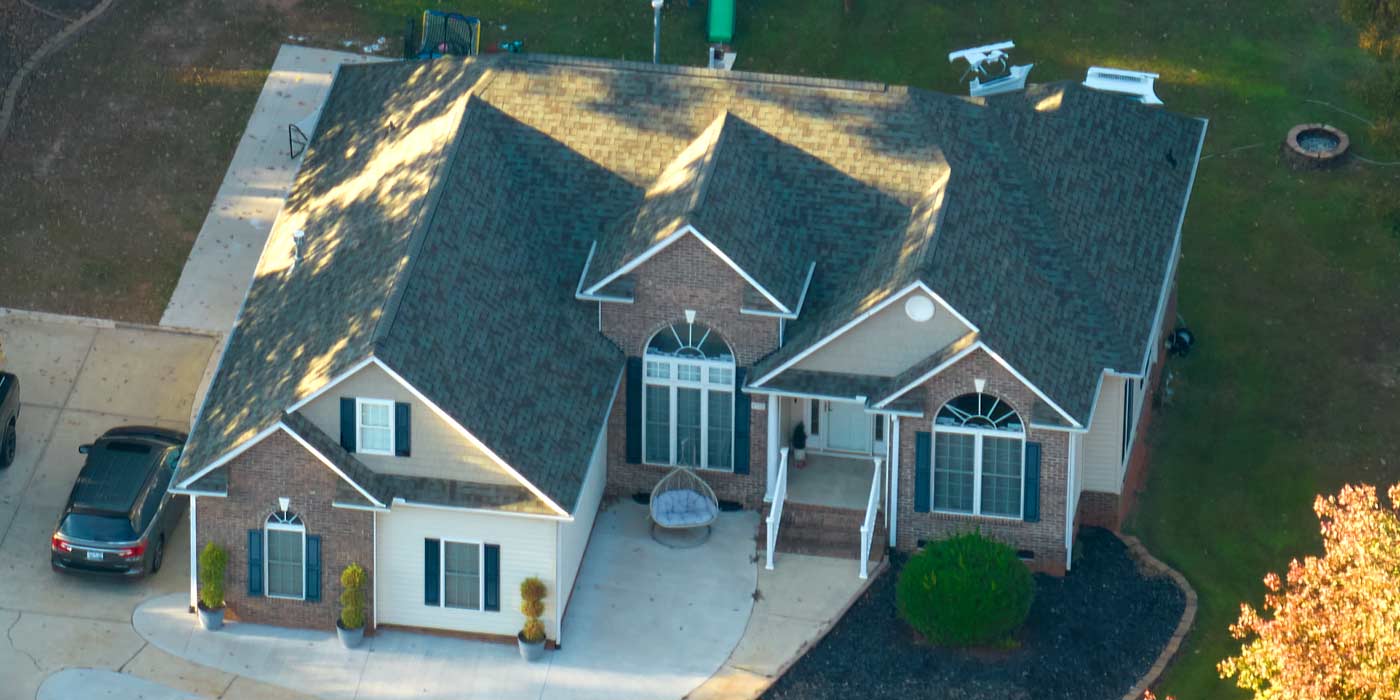 Aerial view of a brick home with a full architectural shingle roof in late-afternoon fall light